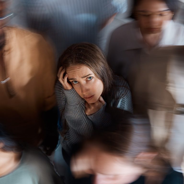 Alone in a room full of people. Shot of a young woman sitting on the floor with people around her