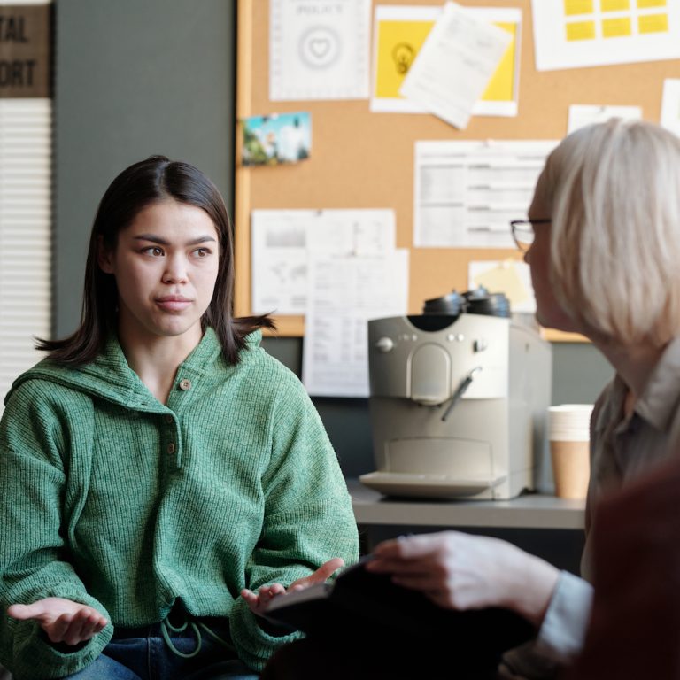 Young serious female patient explaining her psychological problem to psychotherapy specialist and looking at her during session