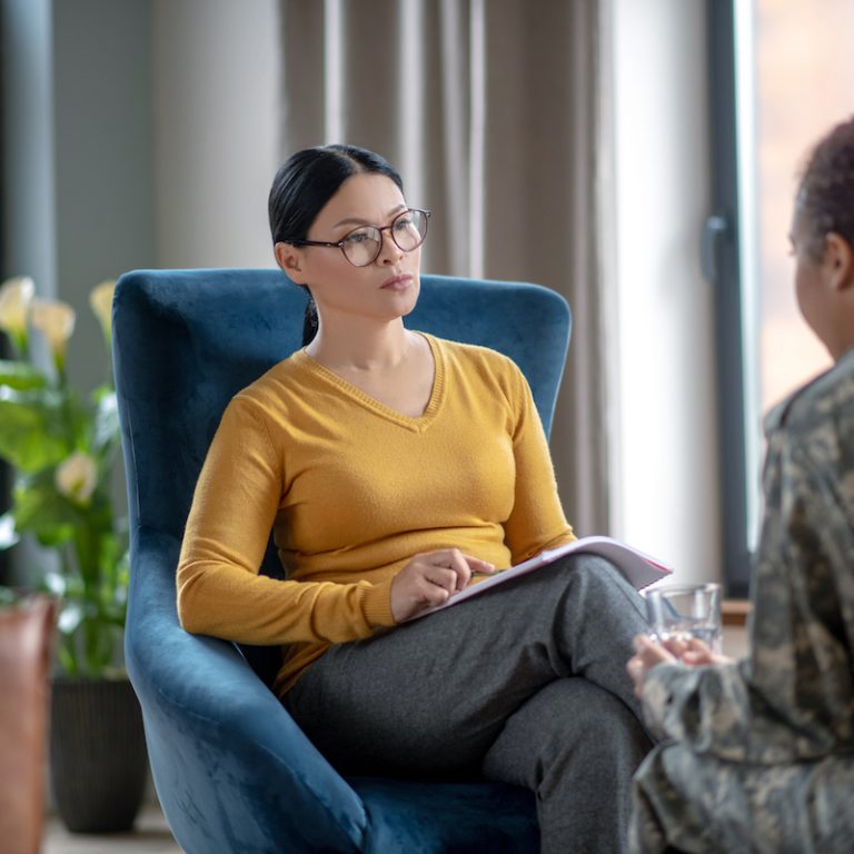 Asian psychoanalyst. Asian dark-haired psychoanalyst listening to woman wearing military uniform